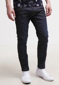 Mörka jeans i slim fit med traditionell femficksdesign och accenttrådar, tillsammans med vita sneakers.
