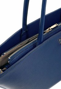 Sac fourre-tout structuré bleu en matériau texturé, doté de deux compartiments zippés, de quincaillerie en argent brillant et de deux poignées.