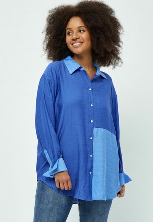 Chemise bleue à manches longues avec un panneau d'accent bleu clair, des poignets contrastés et une coupe décontractée. Texture lisse, design casual.