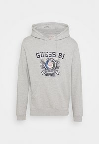 Sudadera gris con capucha que presenta un bolsillo frontal, cordones y un diseño gráfico con "GUESS 81" y acentos florales impresos en azul marino.