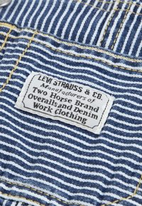 Tissu en denim avec des rayures bleues et blanches, présentant une étiquette blanche avec un texte noir indiquant "LEVI STRAUSS & CO." et des détails sur la marque.