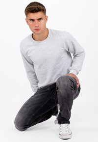 Felpa grigia concollo rotondo e maniche lunghe, abbinata a jeans grigi scuri e sneakers bianche con dettagli rossi. Tessuto morbido, design informale.