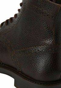 Bottines en cuir brun foncé avec une surface texturée, des détails brogue, des lacets marron et une semelle robuste avec un bord cousu.