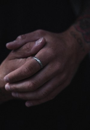 Sidabro žiedas su išsuktos tekstūros, dėvimas ant piršto. Rankos susikibusios kartu, rodant odos atspalvį ir žiedo dizaino ypatybes.