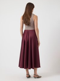 Canottiera beige abbinata a una gonna midi fluida color borgogna. La gonna presenta una texture liscia e l'outfit è completato da tacchi grigi chiari.