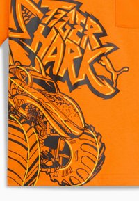 Ryškiai oranžinė marškinė su išraiškinga juoda ir geltona monster truck grafika bei stilizuotu tekstu "Hot Wheels."