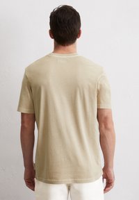 Beige Baumwoll-T-Shirt mit Rundhalsausschnitt, kurzen Ärmeln und lässiger Passform. Die Rückseite zeigt eine glatte Textur mit minimalen Details.