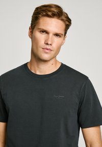 Camiseta de algodón negra con cuello redondo, mangas cortas y un pequeño logo sutil impreso en el pecho. Textura suave, ajuste casual.