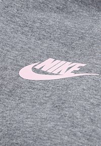 Camiseta de tejido gris con una textura suave que presenta un logo de Nike en rosa visible centrado en el frente, destacando el icónico diseño de swoosh de la marca.