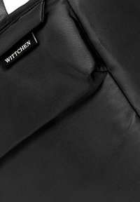 Primo piano di un tessuto nero testurizzato con un piccolo etichetta nera con la scritta "WITTCHEN" cucita in una cucitura.