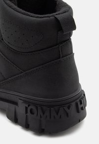 Bottines noires en daim avec col rembourré, tige texturée, marquage « TOMMY HILFIGER » bien visible sur la semelle en caoutchouc, et motif de semelle durable.