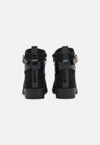 Černé kotníkové boty vyrobené z nubuku a syntetického materiálu, s texturovaným kroko vzorem, zadním poutkem a ozdobným popruhem s přezkou.