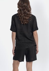 Camicia nera in lino a maniche corte con risvolti e pantaloni corti abbinati. Vestibilità ampia con una superficie texture e una lucentezza sottile.