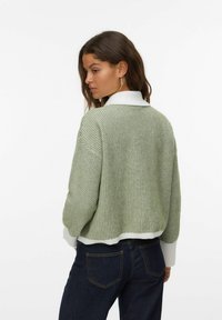 Jasnozielony sweter dziany z białym kołnierzykiem, charakteryzujący się luźnym krojem i teksturowanym wzorem. Dolna krawędź jest biała, prążkowana, w połączeniu z ciemnymi dżinsami.