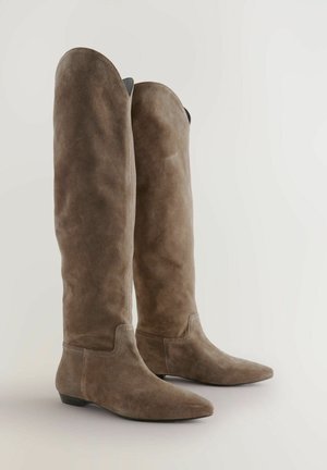 Bottes en daim marron, montantes jusqu'aux genoux, avec un bout pointu, une texture lisse et un accent cousu au niveau de la cheville. Semelle plate.