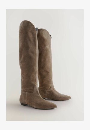 Knee-high, ruskeat mokkasaappaat, joissa on terävä kärki, sileä pinta ja tikattu yksityiskohta nilkassa. Tasapohjainen malli.