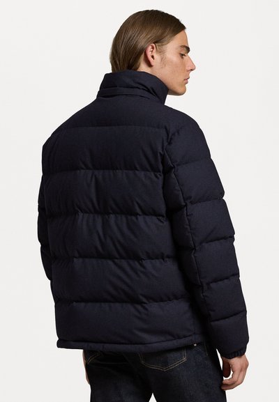 Navy puffer jacket with a high collar, featuring a quilted design and rubberized detailing. Smooth texture, minimalistic design.