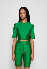 Top crop verde e calções de ciclismo coordenados, feitos de material suave, com mangas curtas, detalhes recortados e costura em contraste vermelha.