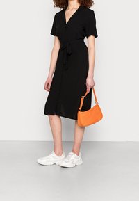 Abito camicia nero a maniche corte con cintura, caratterizzato da bottoni sul davanti. Abbinato a sneaker bianche e una borsa arancione con texture.