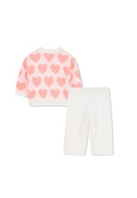 Roze en witte gebreide trui met hartpatronen, gecombineerd met witte geribde broek. Beide stukken hebben zachte texturen en een casual stijl.
