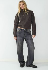 Dunkelbrauner, taillierter Rollkragenpullover, kombiniert mit ausgewaschenen, lockeren, dunklen Jeans und schwarzen Slipschuhen. Einfaches, minimalistisches Design.