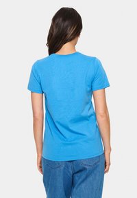 T-shirt en coton bleu ciel à manches courtes et col rond. Texture douce et design simple, associé à un jean en denim bleu clair.