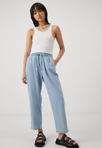 Light blue linen jogger pants with elastic waist and drawstring, paired with a white ribbed tank top and black strappy sandals.