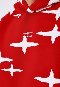 Sudadera roja con grandes patrones de estrellas blancas. Incluye un pequeño logo blanco en el pecho. Fabricada con tela suave y de corte relajado.