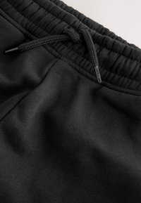 Black sweatpants featuring a textured, soft fabric. Waistband has gathered elastic and a woven drawstring for adjustment.