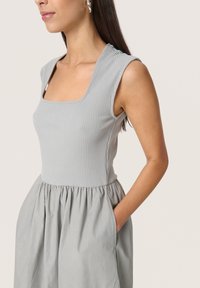 Graues, geripptes Kleid mit quadratischem Ausschnitt und kurzen Ärmeln, ausgestattet mit einem gerafften Rock und seitlichen Taschen. Glatte Stoffstruktur.