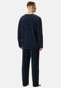 Conjunto de pijamas de forro polar de color azul marino que incluye una parte superior de manga larga a rayas y pantalones sólidos a juego, con un corte holgado y textura suave.