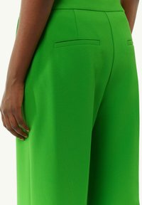 Zielone spodnie z wysokim stanem, wykonane z teksturowanej tkaniny, z dwoma kieszeniami z tyłu i dopasowanym krojem. Gładkie wykończenie i proste linie.