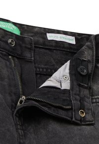 Jeans de mezclilla negra con corte recto. Entre sus características se incluyen una cremallera, cierre con botón y una etiqueta verde. Detalles de bolsillos con herrajes plateados.
