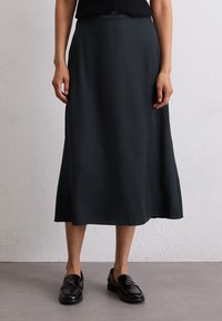 Schwarze, knöchellange Rock aus glattem Stoff, mit einem seitlichen Schlitz und einem schlichten, eleganten Design. Kombiniert mit glänzenden Slippern.