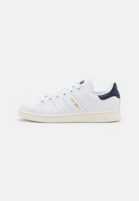 Weiße Leder-Sneaker mit navyfarbenem Fersenakzent, goldfarbenem "Stan Smith"-Logo, perforierten Details und cremefarbener Gummisohle. Klassisches Design.