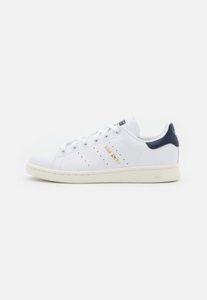 Weiße Leder-Sneaker mit navyfarbenem Fersenakzent, goldfarbenem "Stan Smith"-Logo, perforierten Details und cremefarbener Gummisohle. Klassisches Design.