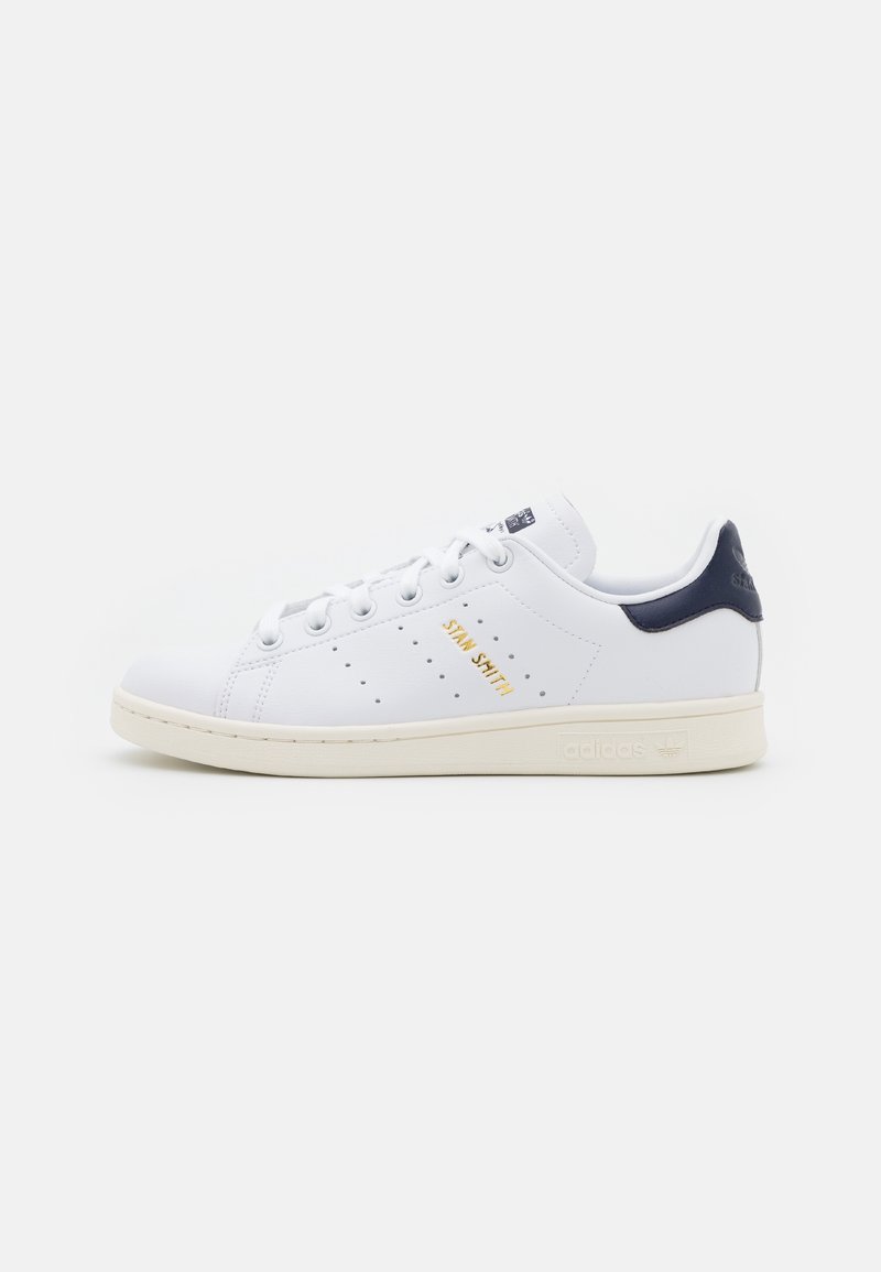 Weiße Leder-Sneaker mit navyfarbenem Fersenakzent, goldfarbenem "Stan Smith"-Logo, perforierten Details und cremefarbener Gummisohle. Klassisches Design.