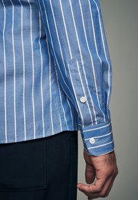 Hellblau gestreiftes Hemd mit weißen vertikalen Linien, mit geknöpften Manschetten, tailliertem Schnitt und glatter Textur.