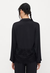Black blouse with long sleeves, satin material, lace trim at the bottom, and a classic collar. Smooth texture throughout the fabric.