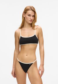 Ensemble bikini noir comprenant un haut court orné d'un galon crème et de fines bretelles, assorti d'un bas taille basse. Texture lisse.