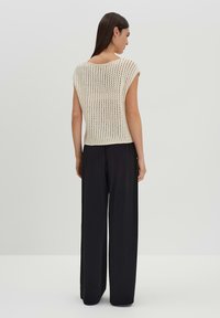 Gebreide top in off-white met een losse, open weving; korte mouwen; gecombineerd met lange, donkere broeken; achteraanzicht toont de ontwerpen van de halslijn en mouwen.