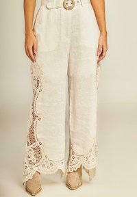 Witte linnen wijde broek met ingewikkelde kantafwerking aan de zijkanten, met een hoge taille en een decoratieve riem met een ronde gesp.