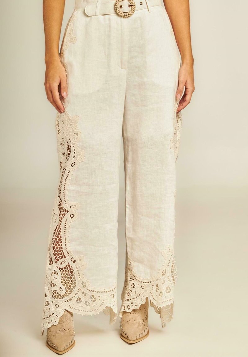 Witte linnen wijde broek met ingewikkelde kantafwerking aan de zijkanten, met een hoge taille en een decoratieve riem met een ronde gesp.