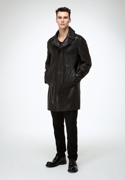 Schwarzer Ledermantel mit klassischem Kragen, Frontreißverschluss und Seitentaschen; kombiniert mit schwarzen Hosen und Schuhen, vor hellem Hintergrund präsentiert.