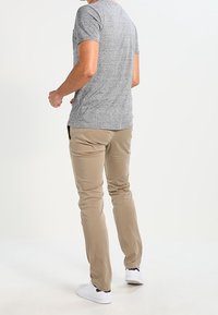 Grå t-shirt med korte ærmer lavet af blødt stof, kombineret med beige chinos og hvide sneakers. Outfit'et har en afslappet pasform og enkelt design.
