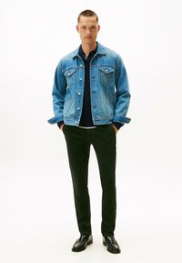 Leren spijkerjack in lichtblauw met voorzakken, knoopsluiting en een klassieke kraag, gecombineerd met donkere broek en zwarte schoenen.