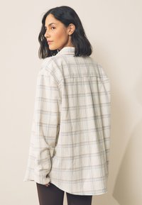 Bílá a světle modrá košile s kostkovaným vzorem, dlouhými rukávy, zapínáním na knoflíky vpředu a volným střihem. Měkká látka s viditelnou texturou a detailem zadního dílu.