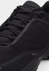 Κοντινό πλάνο μαύρου αθλητικού παπουτσιού με ύφασμα διχτυού, χοντρές στρογγυλές κορδόνια και υφασμένο λαστιχένιο πάτο.