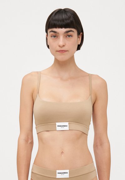 Bralette beige sans coutures avec des fines bretelles, un décolleté carré et une bande de marque en bas. Tissu doux avec une texture lisse.