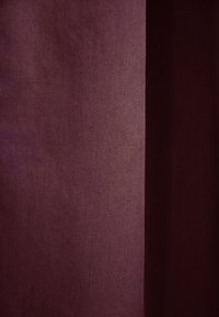 Bordowa tkanina o gładkiej fakturze i subtelnym połysku, z różnicami w odcieniu na powierzchni. Szew biegnący pionowo po jednej stronie.